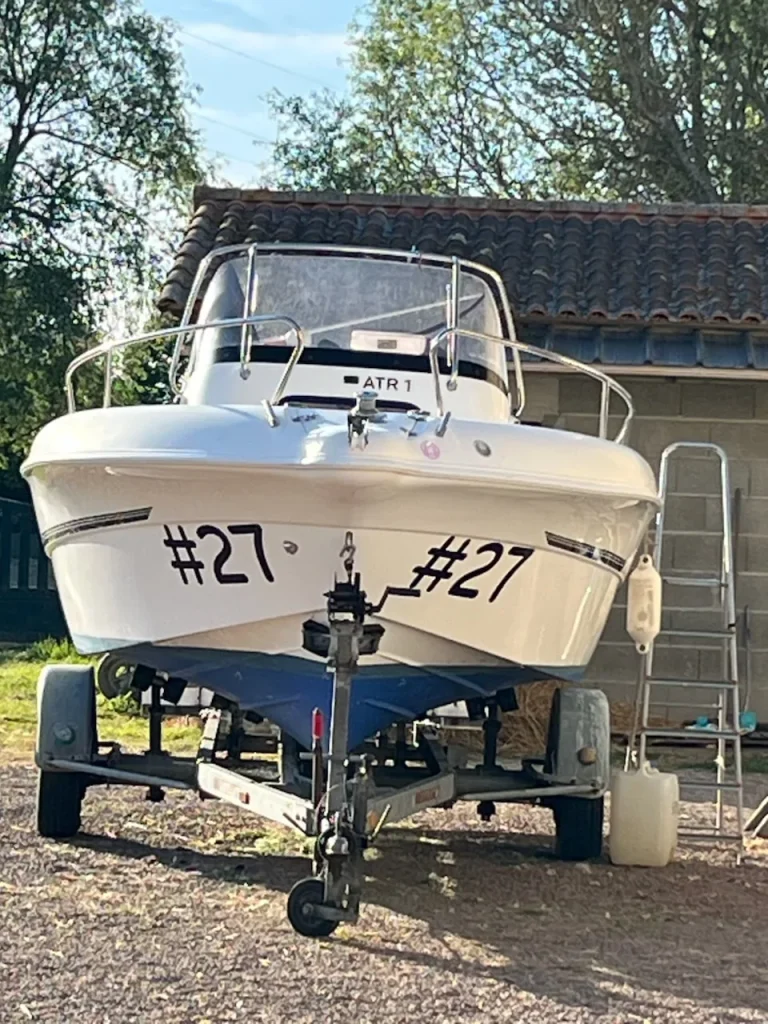Bateau à moteur blanc sur sa remorque, le numéro 27 posé en adhésif noir de chaque côté de la coque