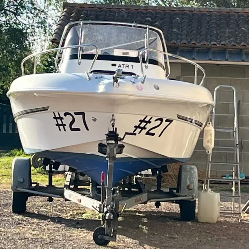 Bateau à moteur blanc sur sa remorque, le numéro 27 posé en adhésif noir de chaque côté de la coque
