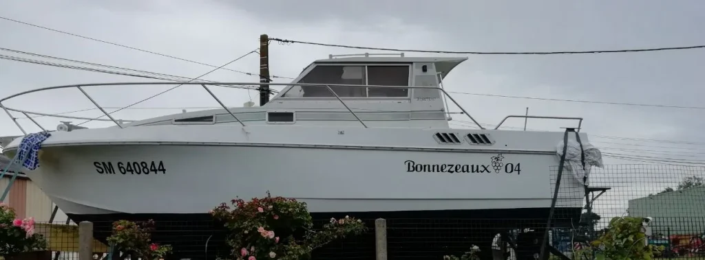Bateau de plaisance blanc sur son ber, nom « Bonnezeaux 04 » et immatriculation en adhésif sur la coque
