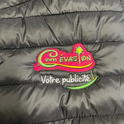 Logo Com Évasion « Votre publicité ! » brodé en rose, vert et blanc sur un bodywarmer noir