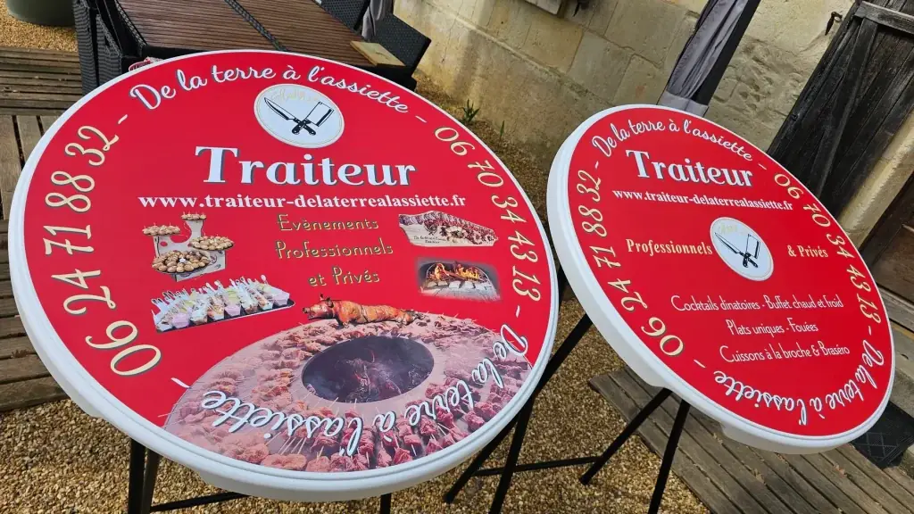 Deux mange-debout rouges « De la terre à l’assiette, Traiteur » avec photos de plats