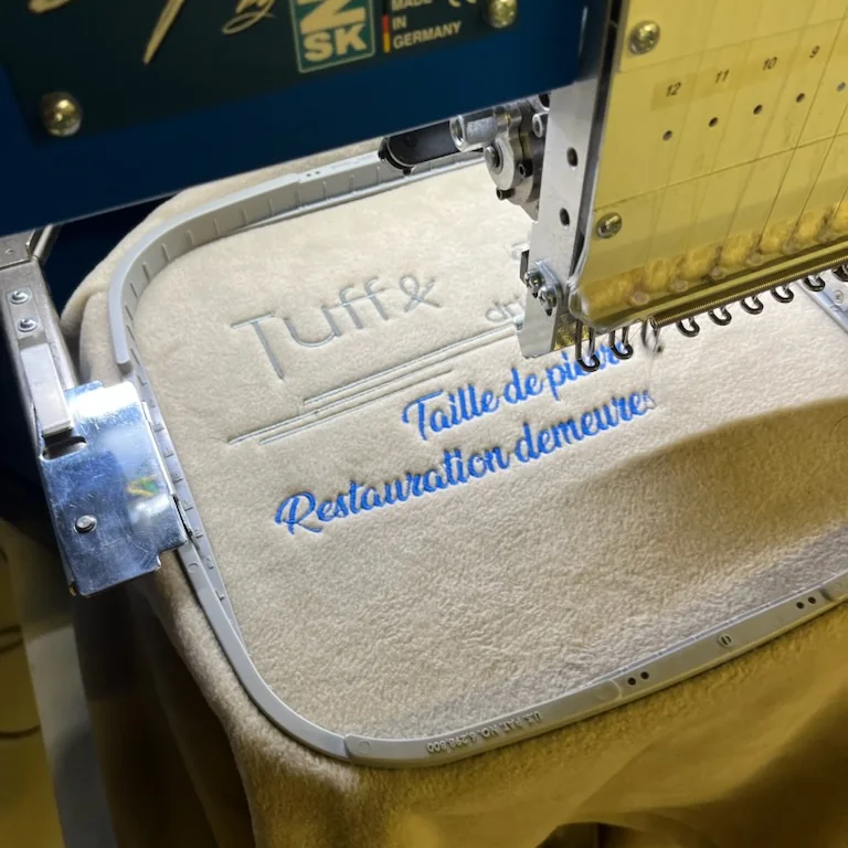 Machine à broder professionnelle brodant « Tuff & Art, taille de pierre » sur une micropolaire beige