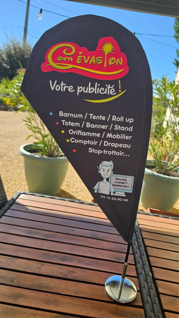 Mini oriflamme noire au logo Com Évasion posée sur une table de jardin