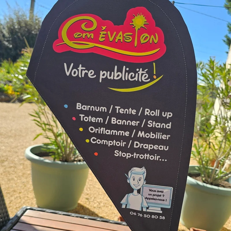 Mini oriflamme noire au logo Com Évasion posée sur une table de jardin
