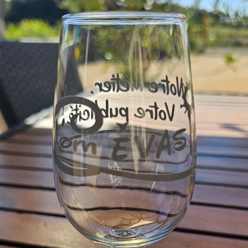 Verre à vin marqué « Votre métier, votre publicité, Com Évasion » posé sur une table en bois