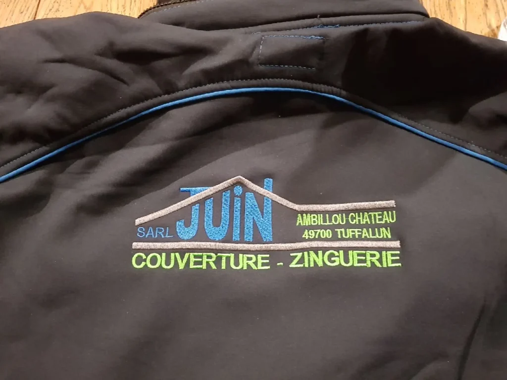 Dos d’une veste noire brodé du logo SARL Juin, couverture zinguerie, en bleu, vert et gris