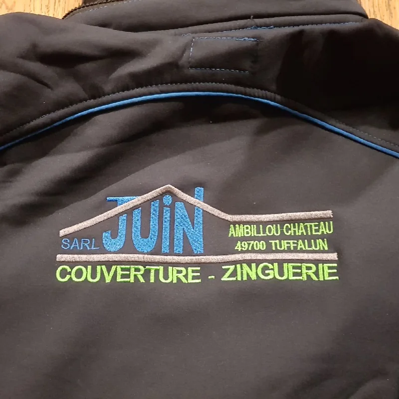 Dos d’une veste noire brodé du logo SARL Juin, couverture zinguerie, en bleu, vert et gris