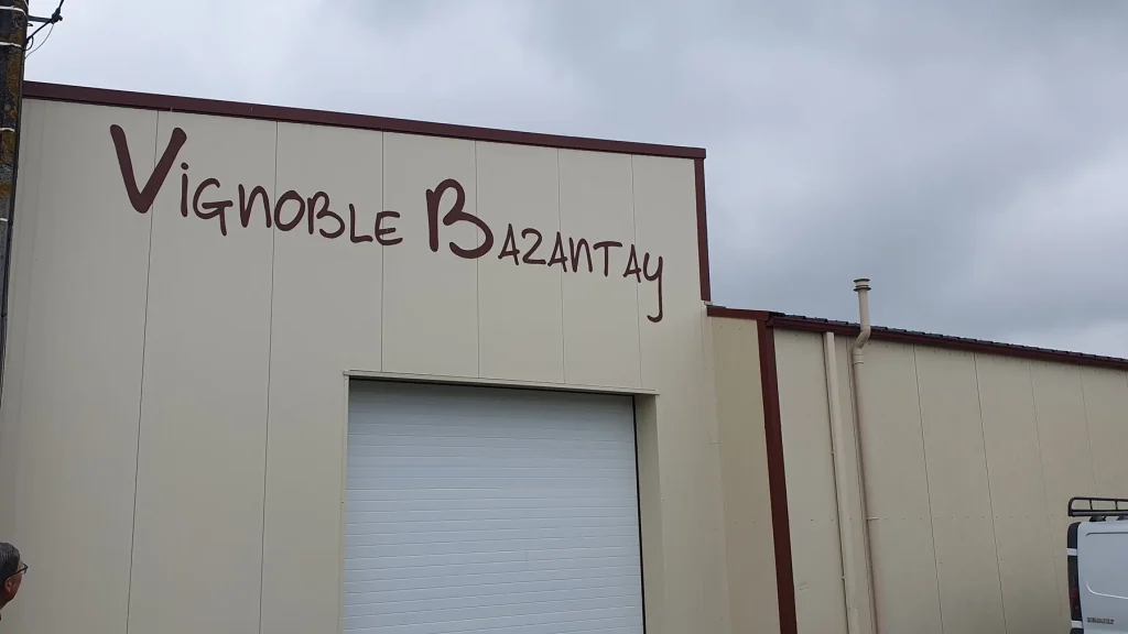 Façade beige avec le nom « Vignoble Bazantay » en grandes lettres découpées bordeaux