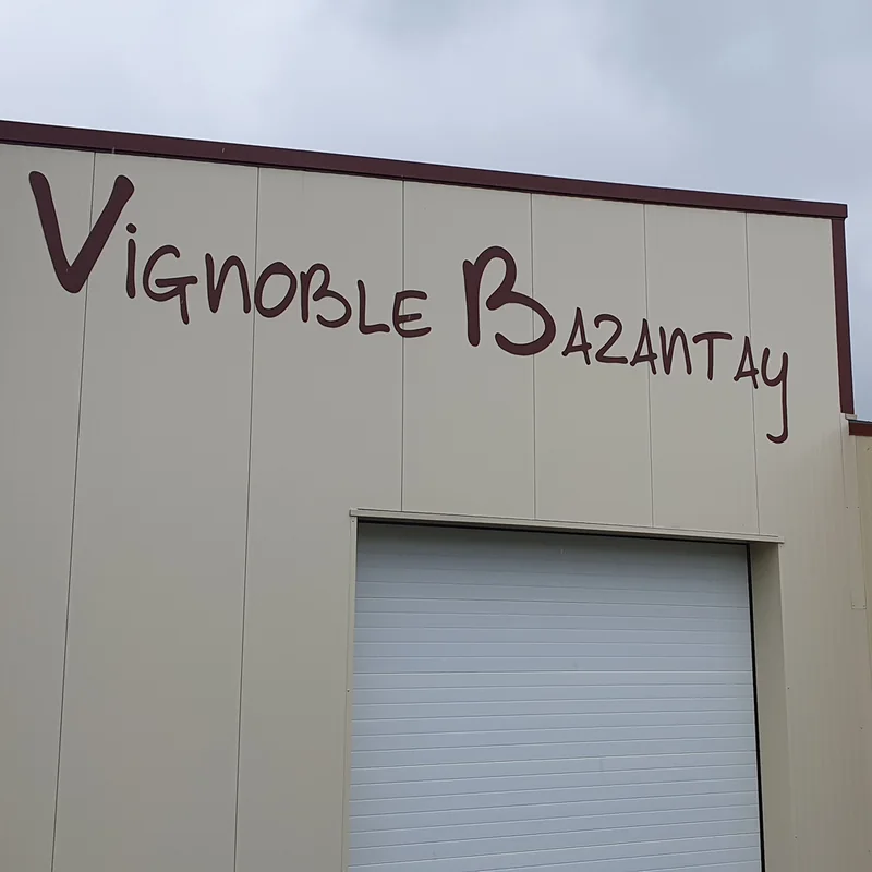 Façade beige avec le nom « Vignoble Bazantay » en grandes lettres découpées bordeaux