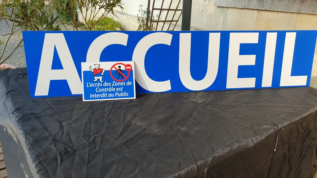 Grand panneau bleu « Accueil » en lettres blanches avec une plaque d’interdiction au public