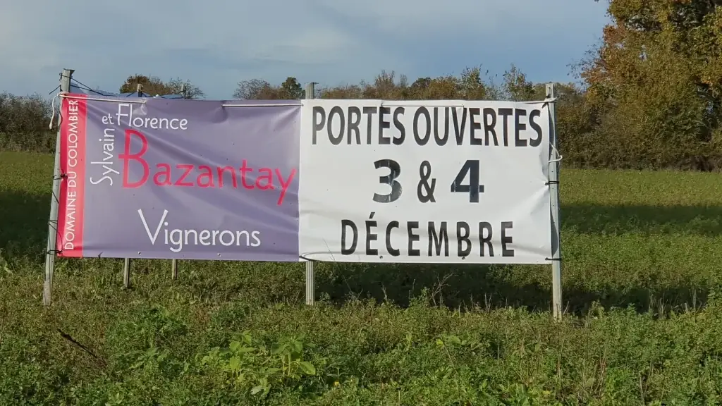 Banderole « Sylvain et Florence Bazantay, vignerons, portes ouvertes 3 et 4 décembre » tendue au bord d’un champ