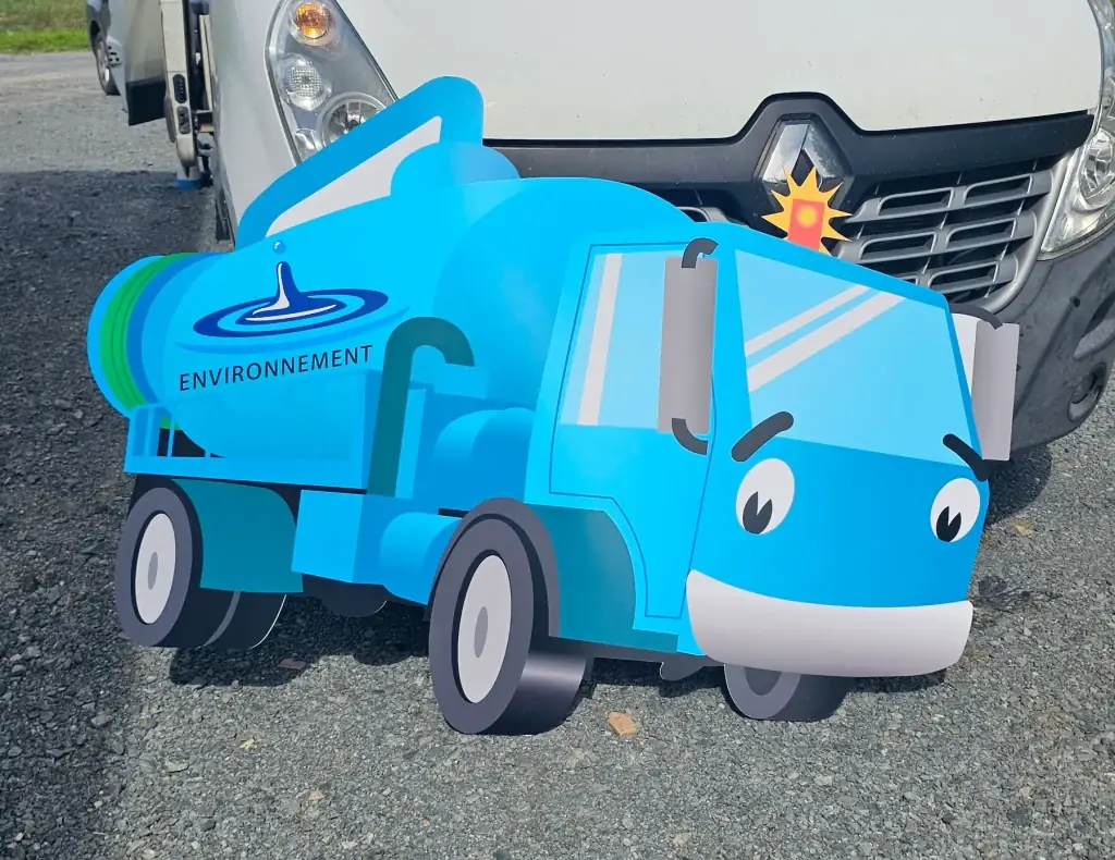 Panneau Dibond découpé en forme de camion de vidange bleu souriant, posé devant un utilitaire