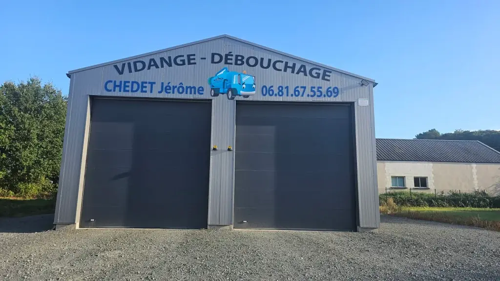 Bâtiment en bardage gris avec l’enseigne « Vidange, débouchage, Chedet Jérôme » et son camion découpé