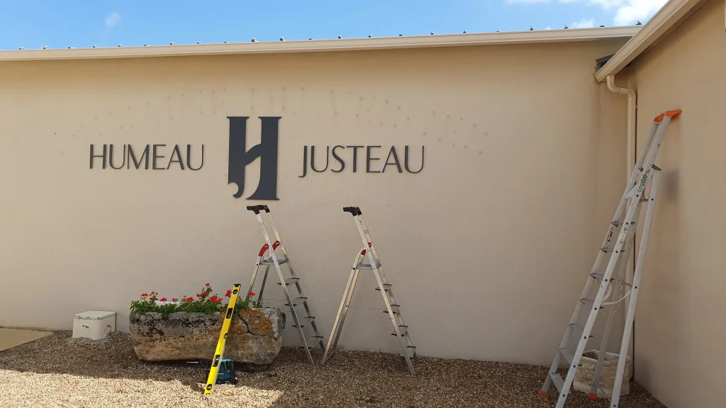 Enseigne en lettres découpées Humeau Justeau posée sur un mur crème, escabeaux encore en place