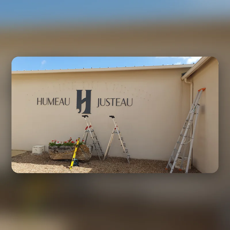 Enseigne en lettres découpées Humeau Justeau posée sur un mur crème, escabeaux encore en place