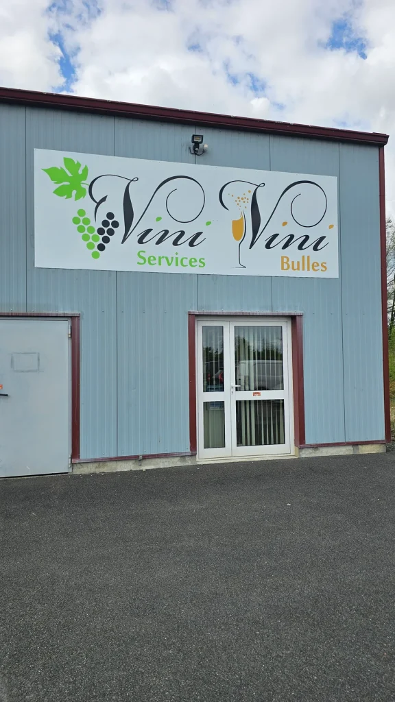 Façade en bardage avec le panneau « Vini Services, Vini Bulles » et une grappe de raisin