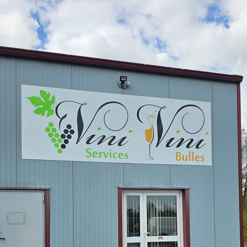 Façade en bardage avec le panneau « Vini Services, Vini Bulles » et une grappe de raisin