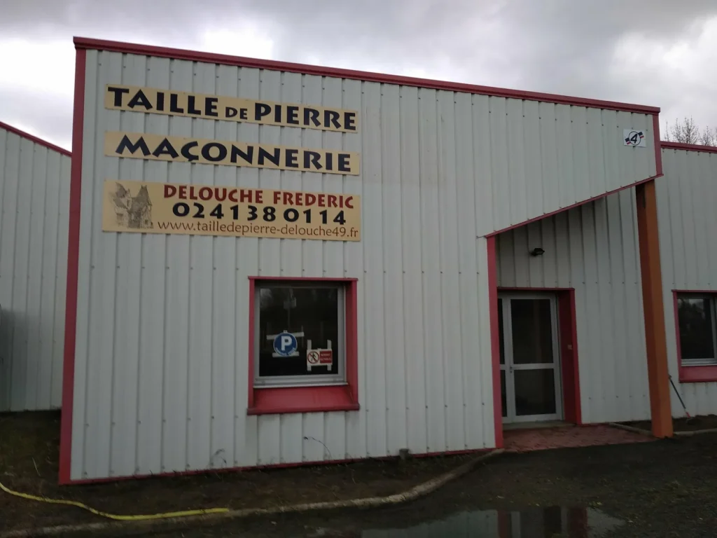 Panneau « Taille de pierre, maçonnerie, Delouche Frédéric » sur la façade d’un bâtiment en bardage
