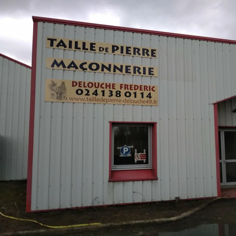 Panneau « Taille de pierre, maçonnerie, Delouche Frédéric » sur la façade d’un bâtiment en bardage