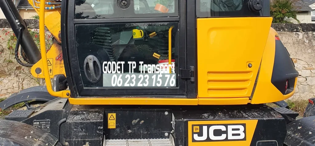 Pelle JCB jaune avec le lettrage « Godet TP Transport » et le numéro sur la vitre de la cabine