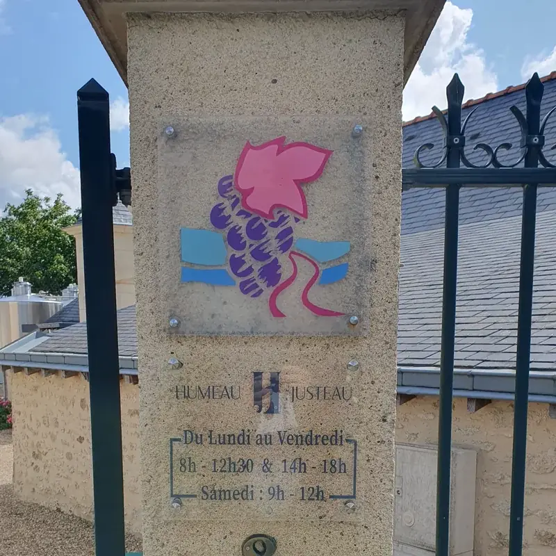 Plaque transparente avec une grappe de raisin et les horaires du domaine Humeau Justeau sur un pilier en pierre