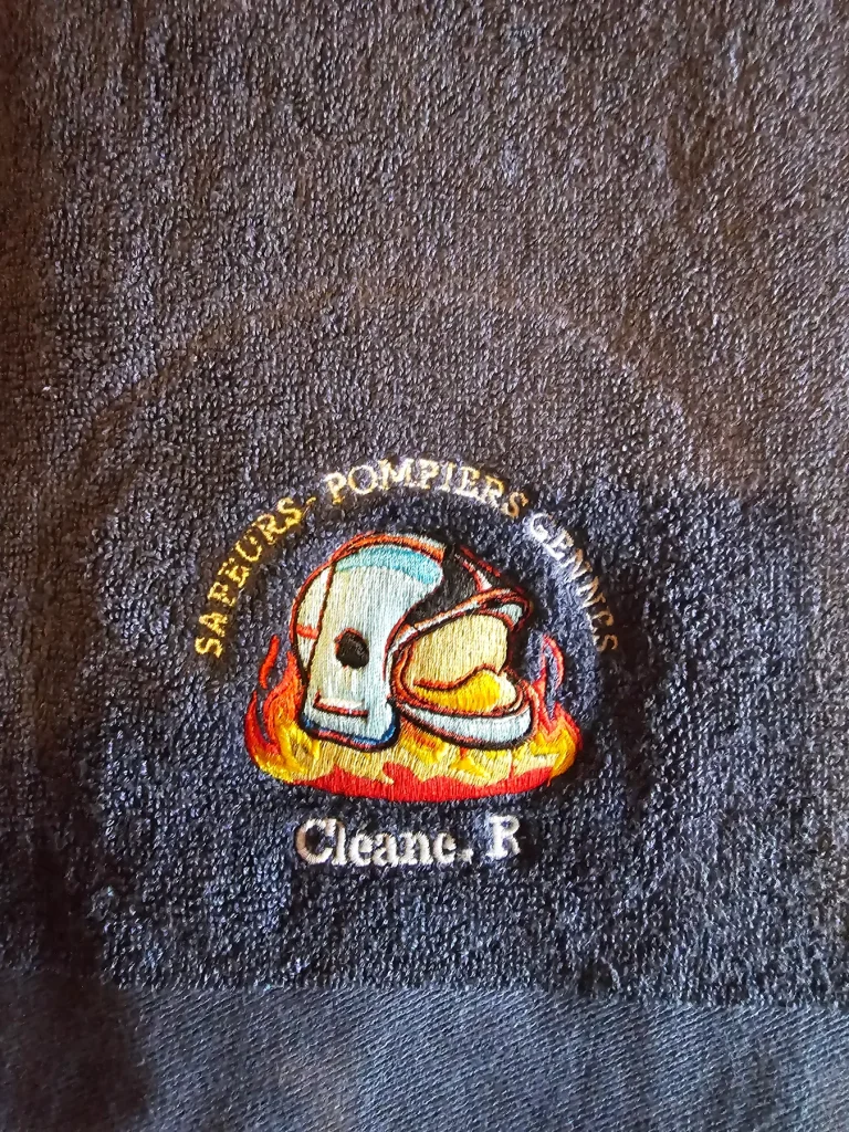 Logo des sapeurs-pompiers de Gennes brodé sur un drap de bain gris : casque et flammes