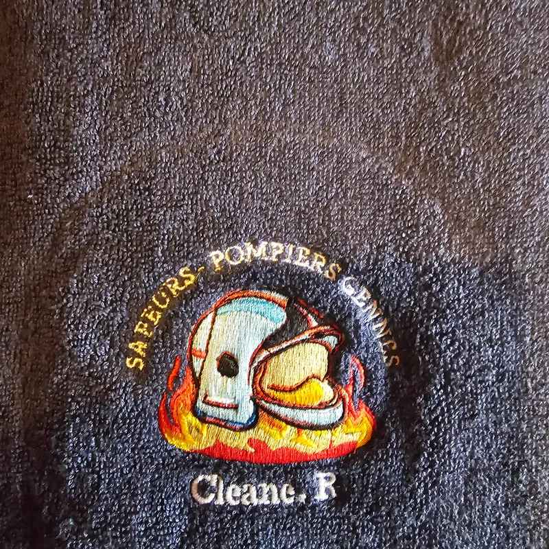 Logo des sapeurs-pompiers de Gennes brodé sur un drap de bain gris : casque et flammes
