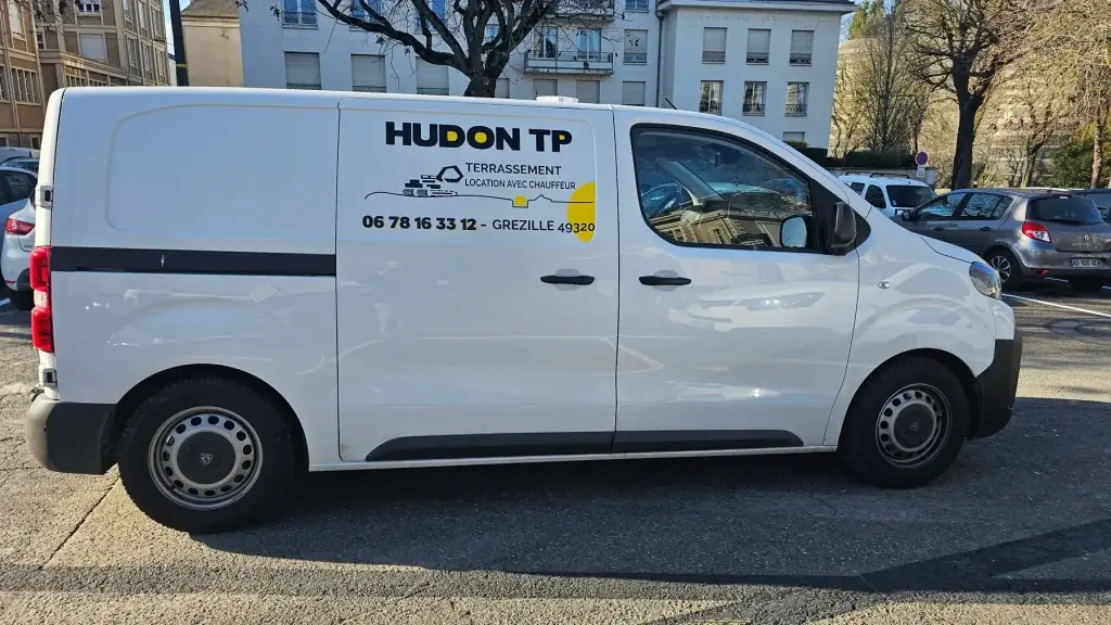 Utilitaire blanc marqué au logo Hudon TP, terrassement, sur la portière arrière