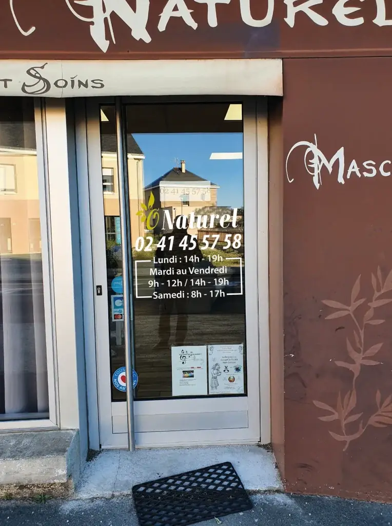Porte vitrée du salon O Naturel avec son logo, son numéro et ses horaires en lettrage adhésif blanc