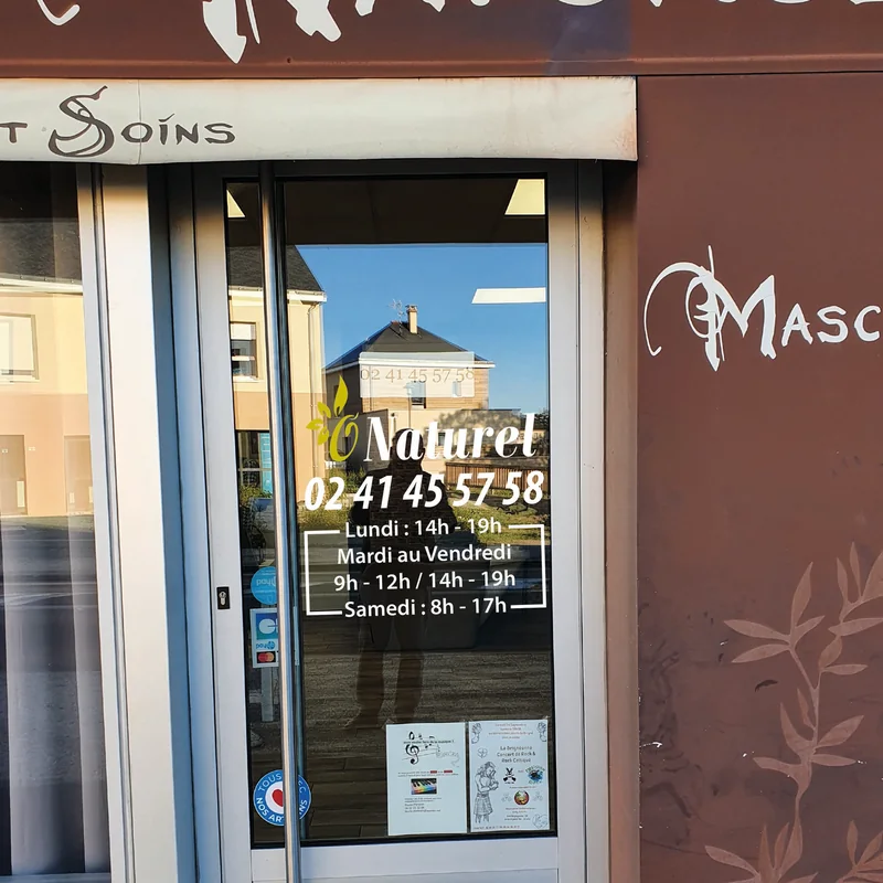 Porte vitrée du salon O Naturel avec son logo, son numéro et ses horaires en lettrage adhésif blanc